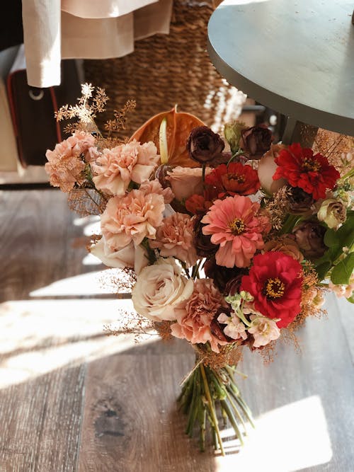 High angle of bunch of fresh red and pink flowers with ribbon placed on wooden floor under table