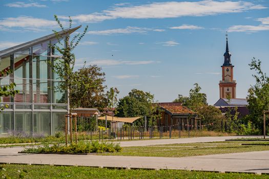 A modern glass building contrasts with a historic church tower under a clear summer sky.
