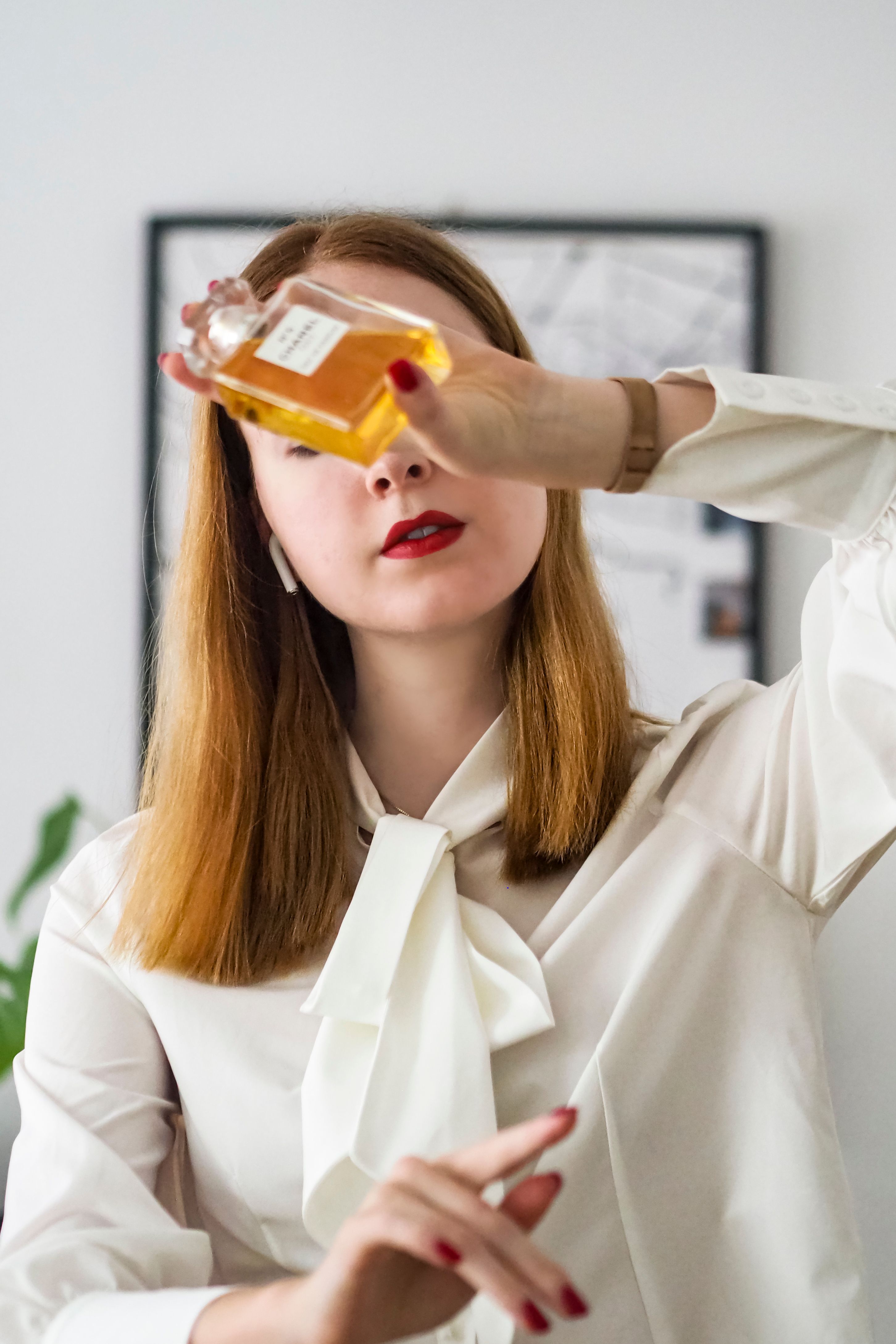 Mulher estilosa em blusa branca segurando frasco de perfume em um cenário moderno parisiense. Chique e elegante.
