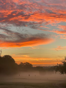 Vivid autumn sunrise with orange clouds over a misty golf course in Sheffield, UK.