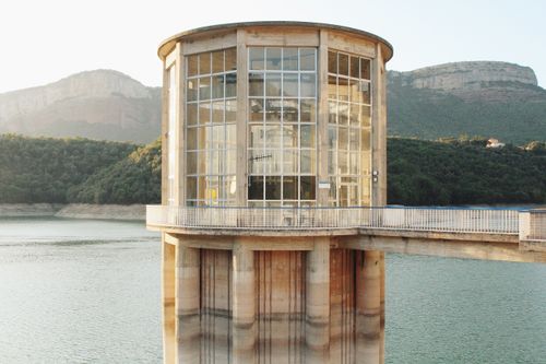 Free A glass structure on a pier over a serene lake in Vic, Spain, with surrounding hills. Stock Photo