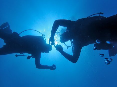 Silhouette of two scuba divers sharing a moment underwater in a bright blue ocean scene.