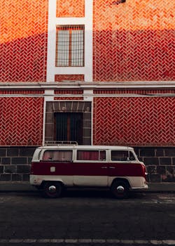 A classic red and white VW camper van parked beside a vibrant textured wall under warm lighting.
