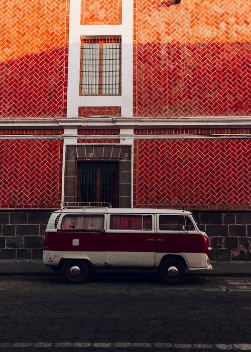 Free A classic red and white VW camper van parked beside a vibrant textured wall under warm lighting. Stock Photo