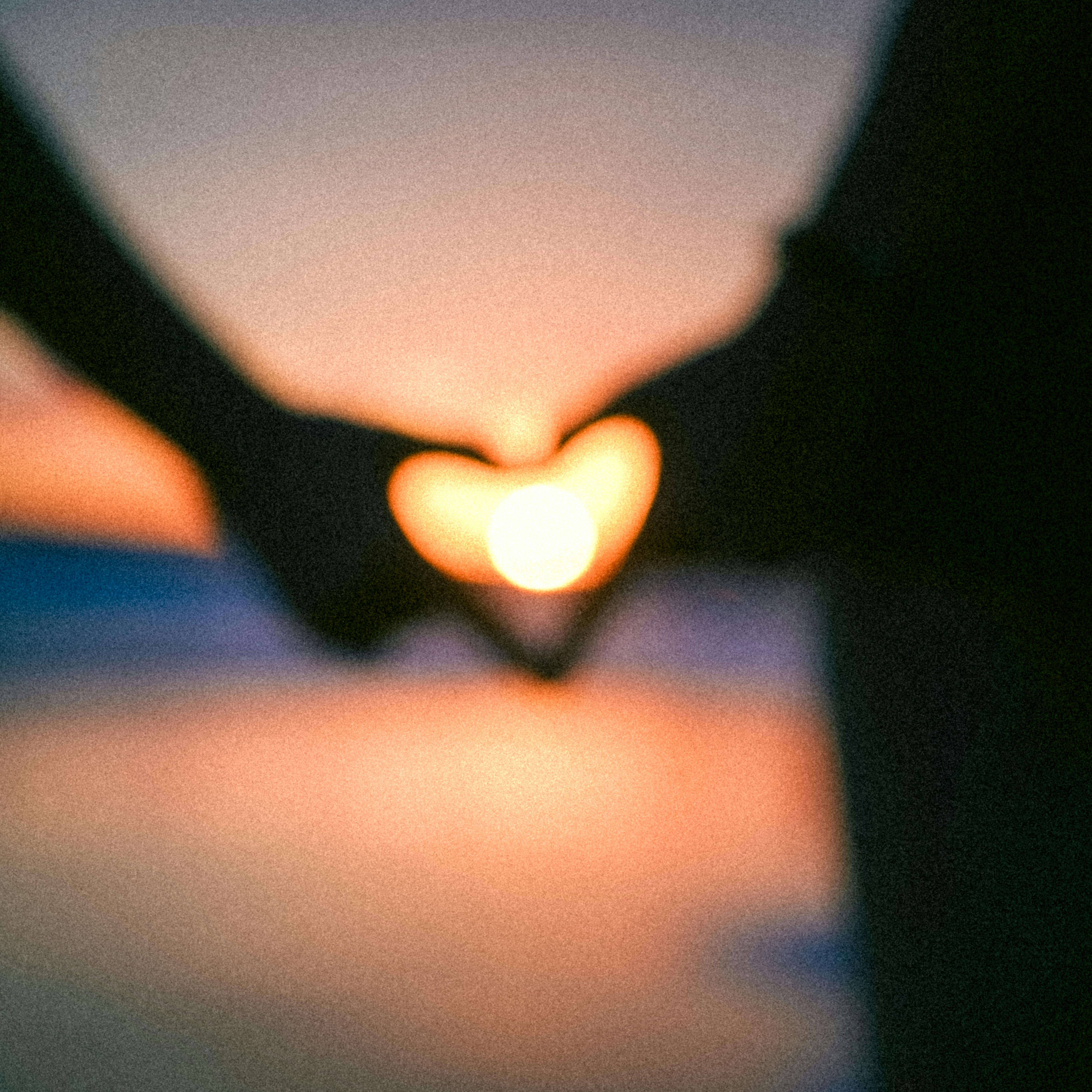 A couple creates a heart silhouette at sunset by the beach, symbolizing love.