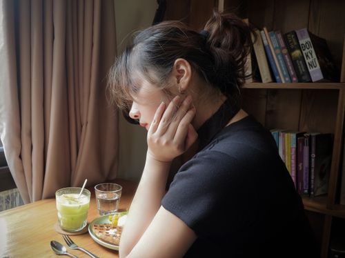 Free Young woman deep in thought in a cozy café, surrounded by books and a warm ambiance. Stock Photo