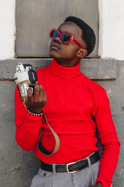 Stylish man with a Canon EOS camera wearing a red turtleneck and sunglasses, outdoors.