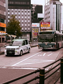 Vibrant city street view in Japan featuring a taxi and a city bus amidst modern buildings.