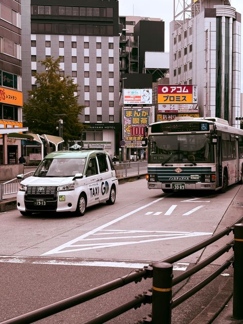 Free Vibrant city street view in Japan featuring a taxi and a city bus amidst modern buildings. Stock Photo
