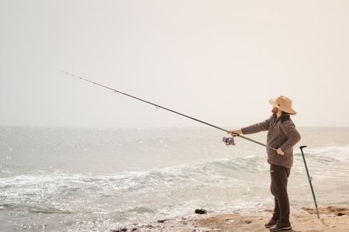 Free A man fishing with a rod by the sea, enjoying a sunny day on the beach. Stock Photo