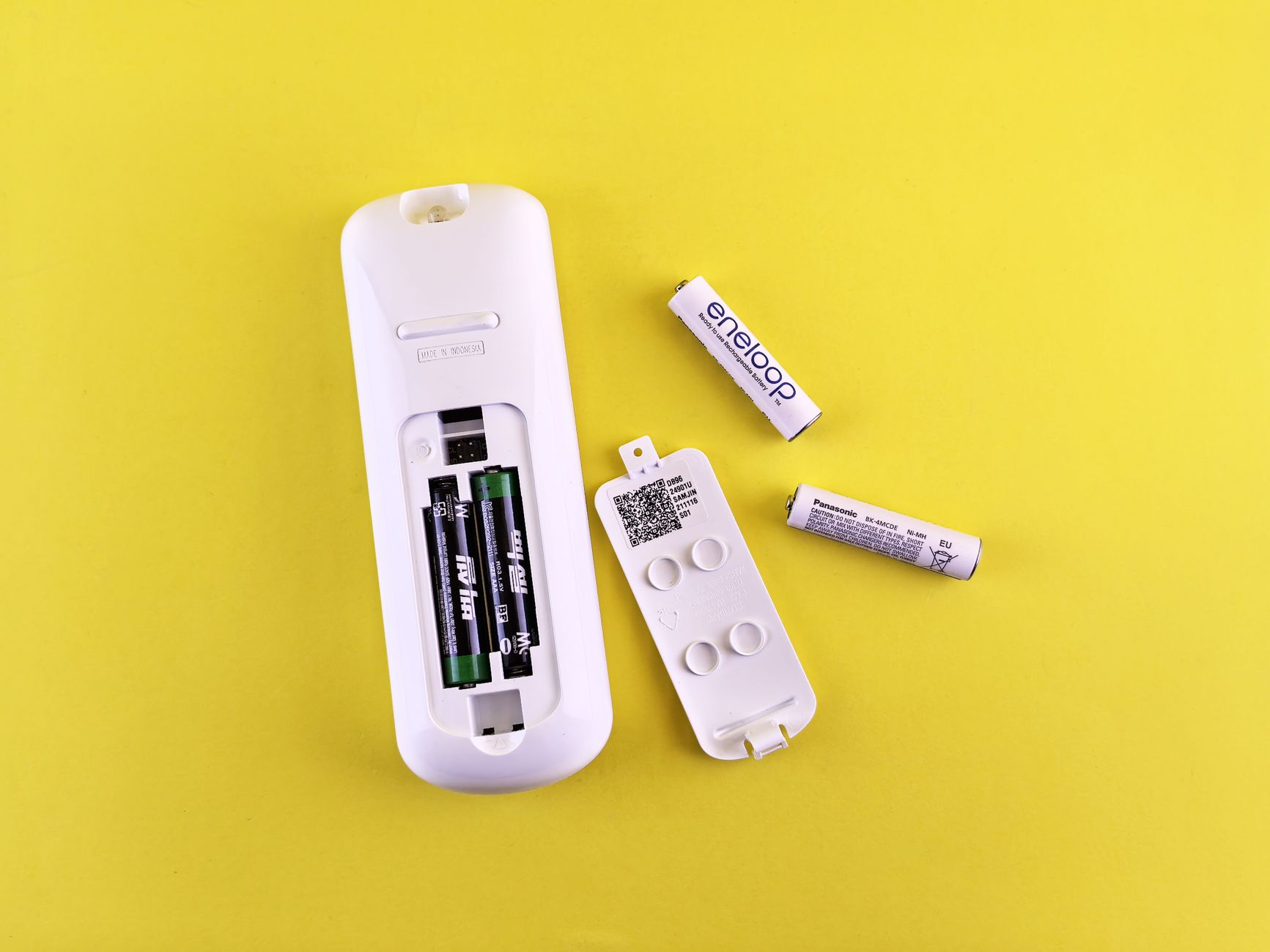 Close-up of remote control and batteries on vibrant yellow surface.
