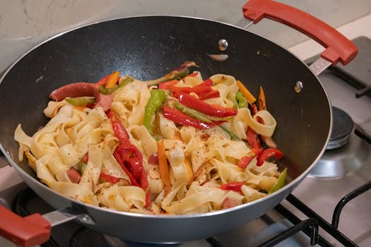 Delicious pasta mixed with vibrant vegetables in a frying pan on the stove.