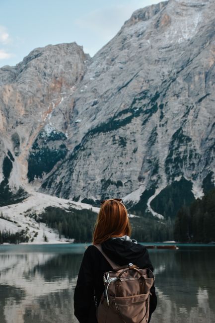 A woman with a backpack enjoys a tranquil view of a mountain lake.