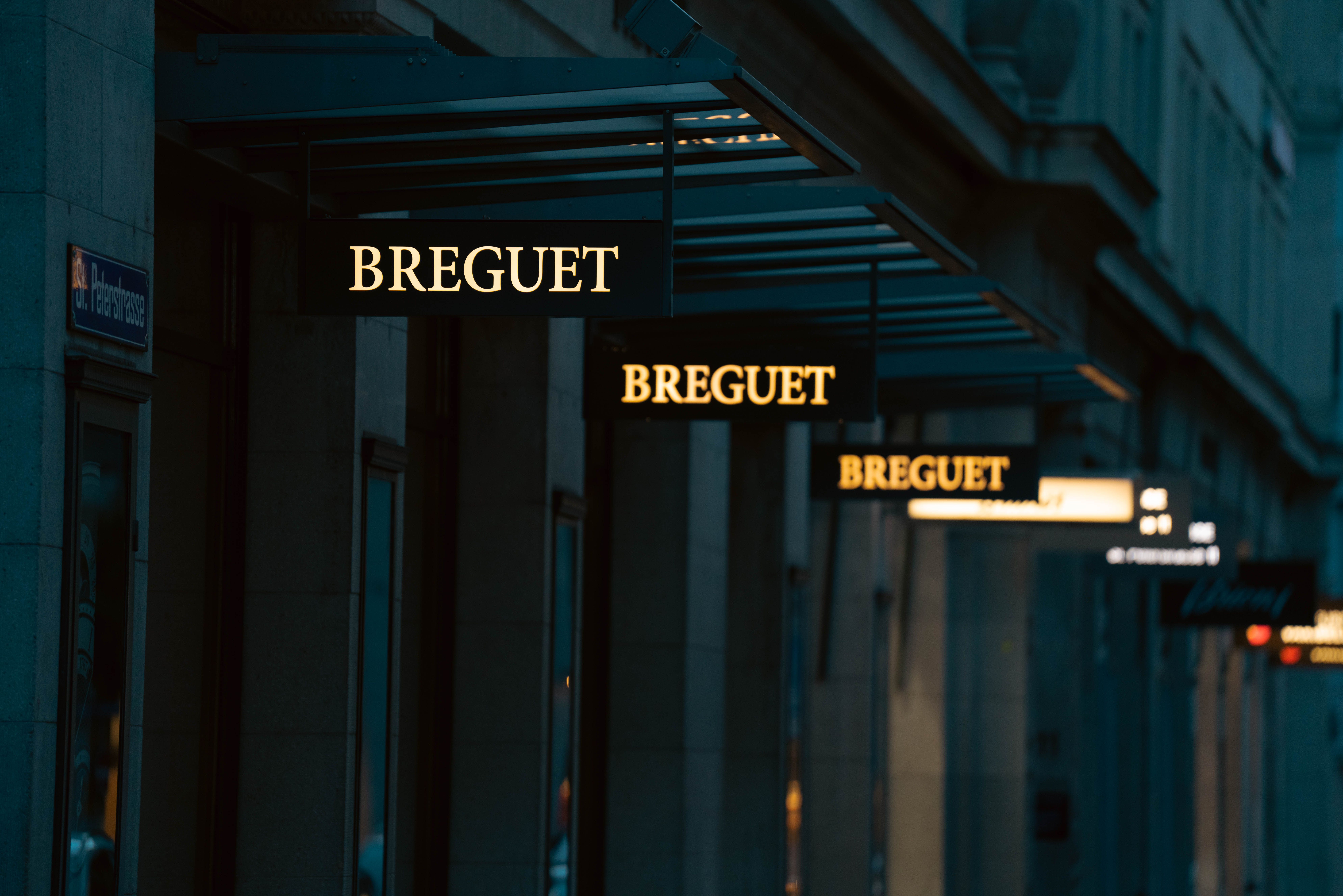 A display of Breguet signs on a city street at dusk, highlighting luxury retail ambiance.