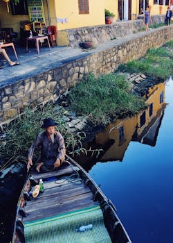 老人驾着一艘木船沿运河航行，映衬出岸边建筑的活力