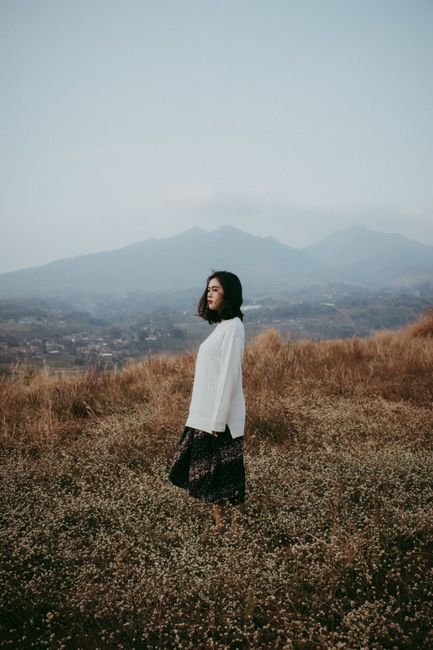 Woman standing in a serene meadow, Bandung, Indonesia, with mountains in the background.