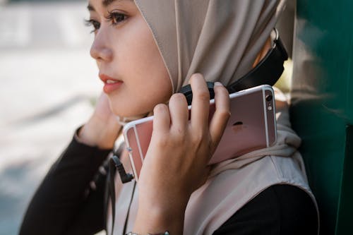 Bezpłatne Kobieta Ubrana W Beżowy Hidżab, Trzymając Smartfon Apple I Phone Zdjęcie z galerii