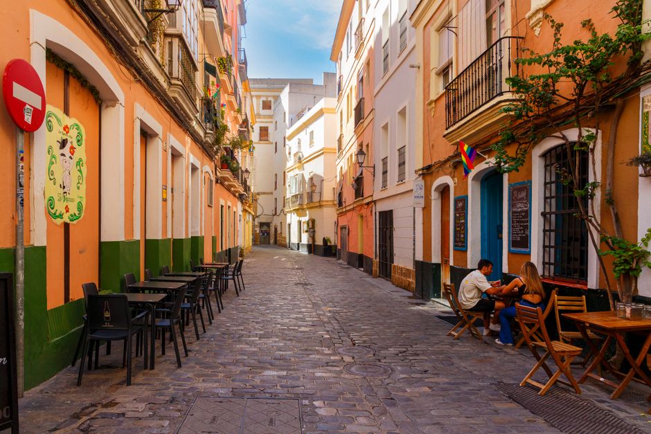Quiet European street with colorful buildings, outdoor cafe seating, and people enjoying a sunny day.