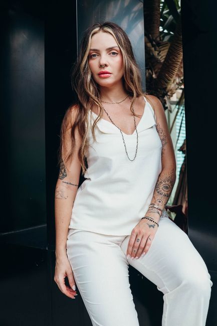 Confident woman in a white outfit posing outdoors with tattoos and jewelry.