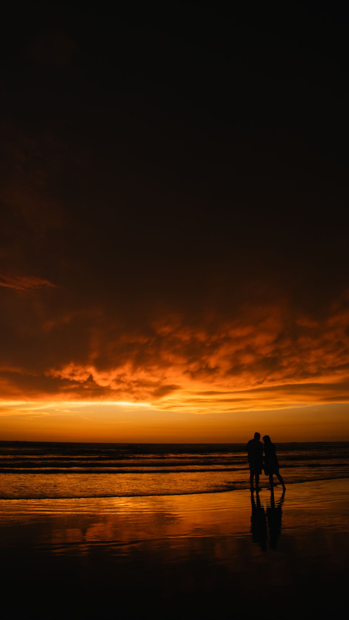 A couple walking on a Cornish beach at sunset