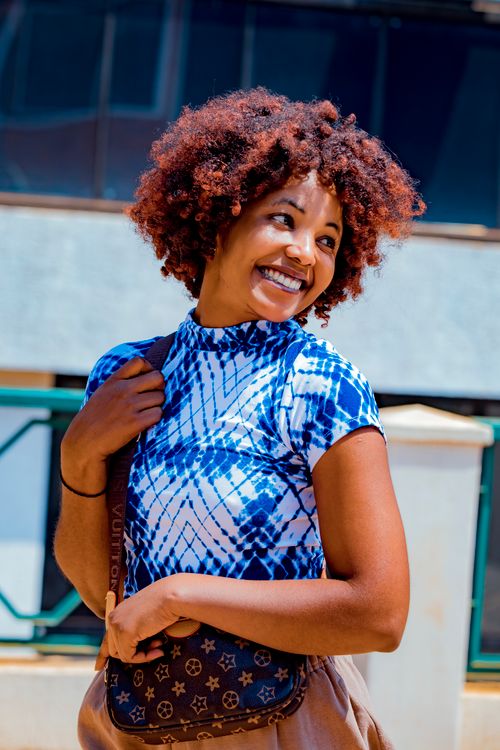 Free Cheerful woman with curly hair smiling outdoors in vibrant sunlight. Stock Photo