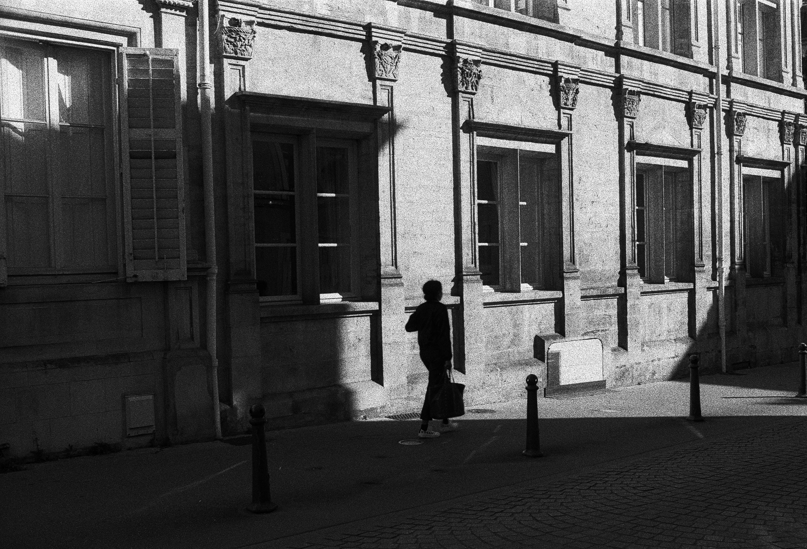 A black and white photo captures a person walking by a historic building in Nancy, France.