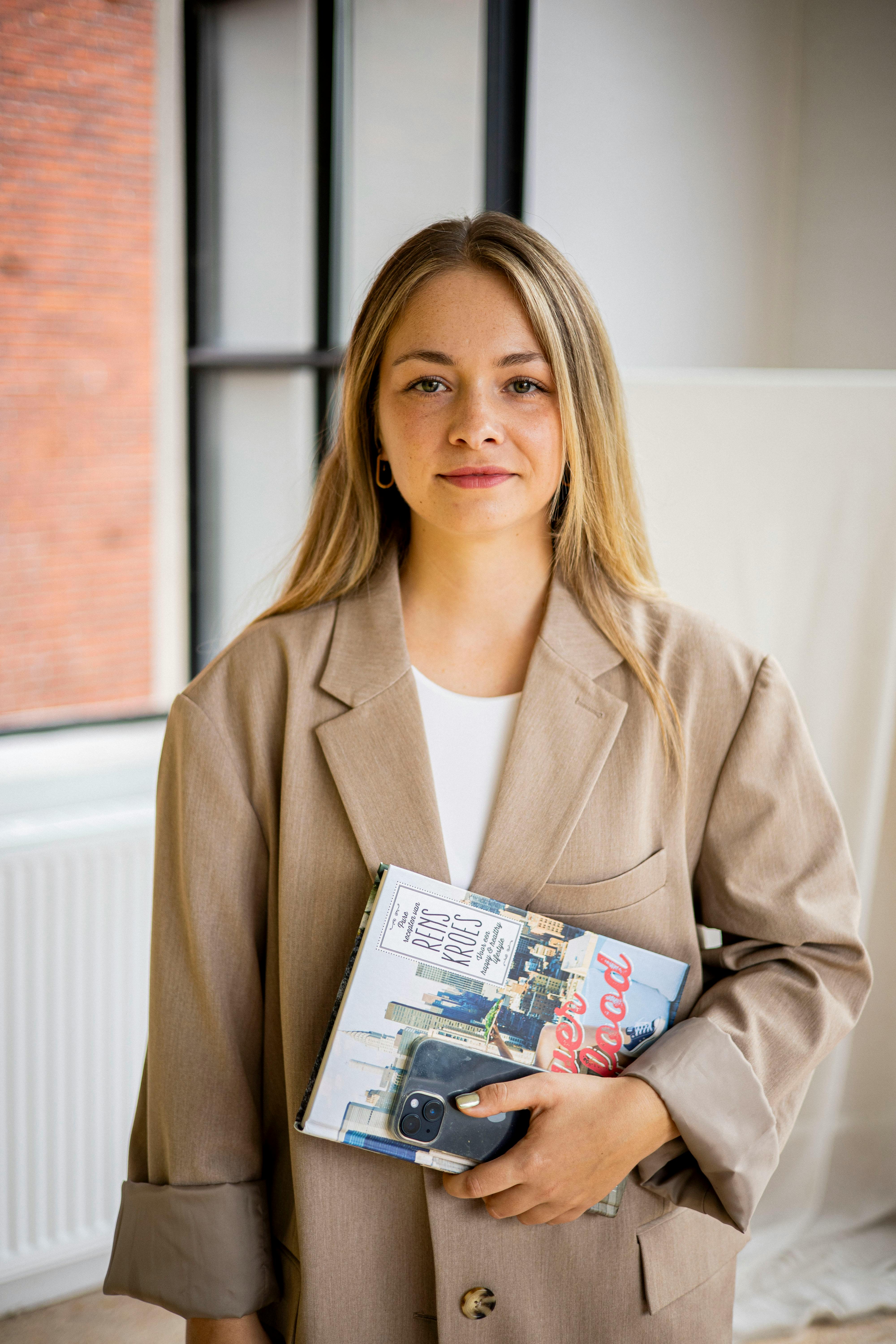Confident young woman holding books in a stylish office setting.