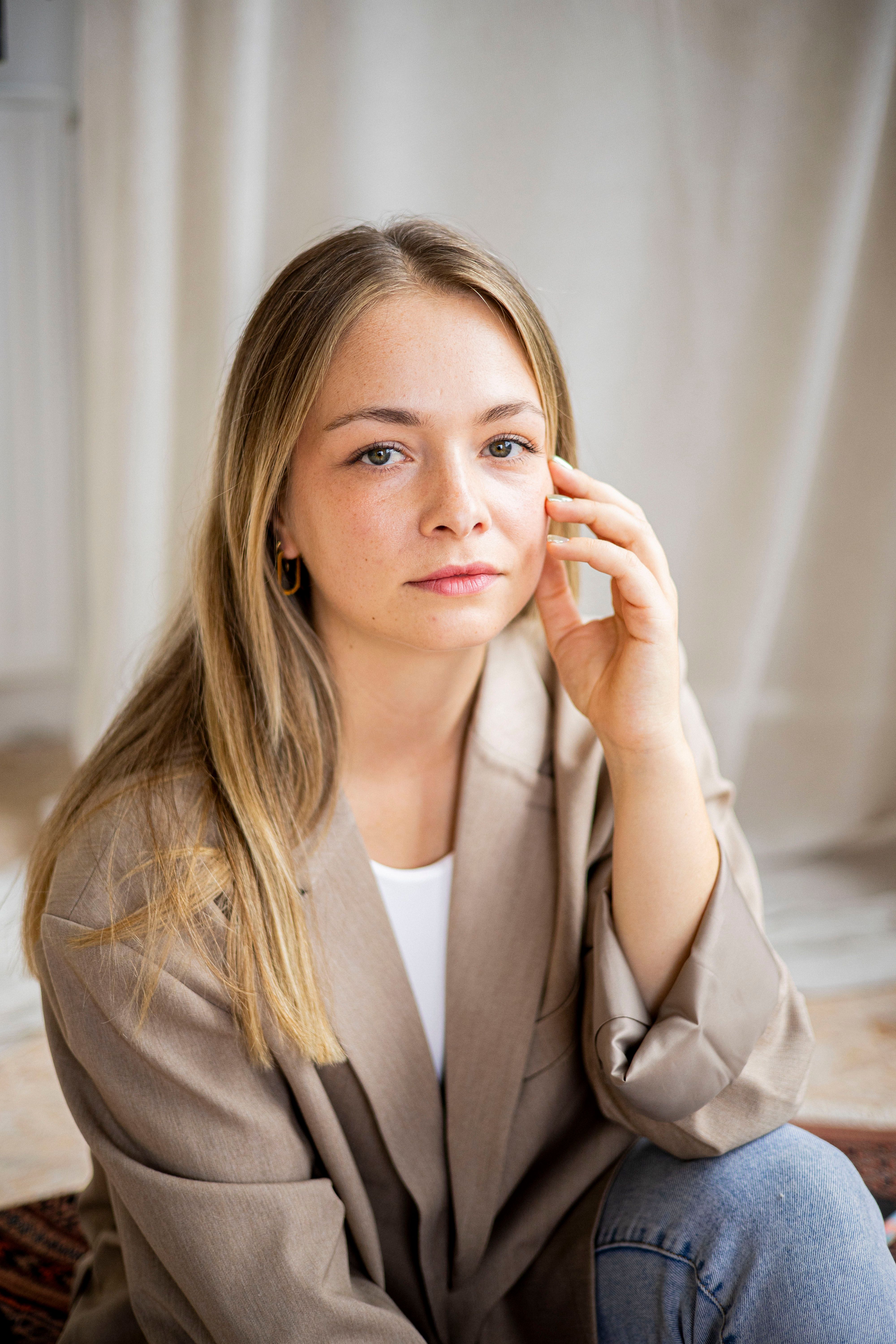 Casual portrait of a woman in a beige blazer with a thoughtful expression indoors.