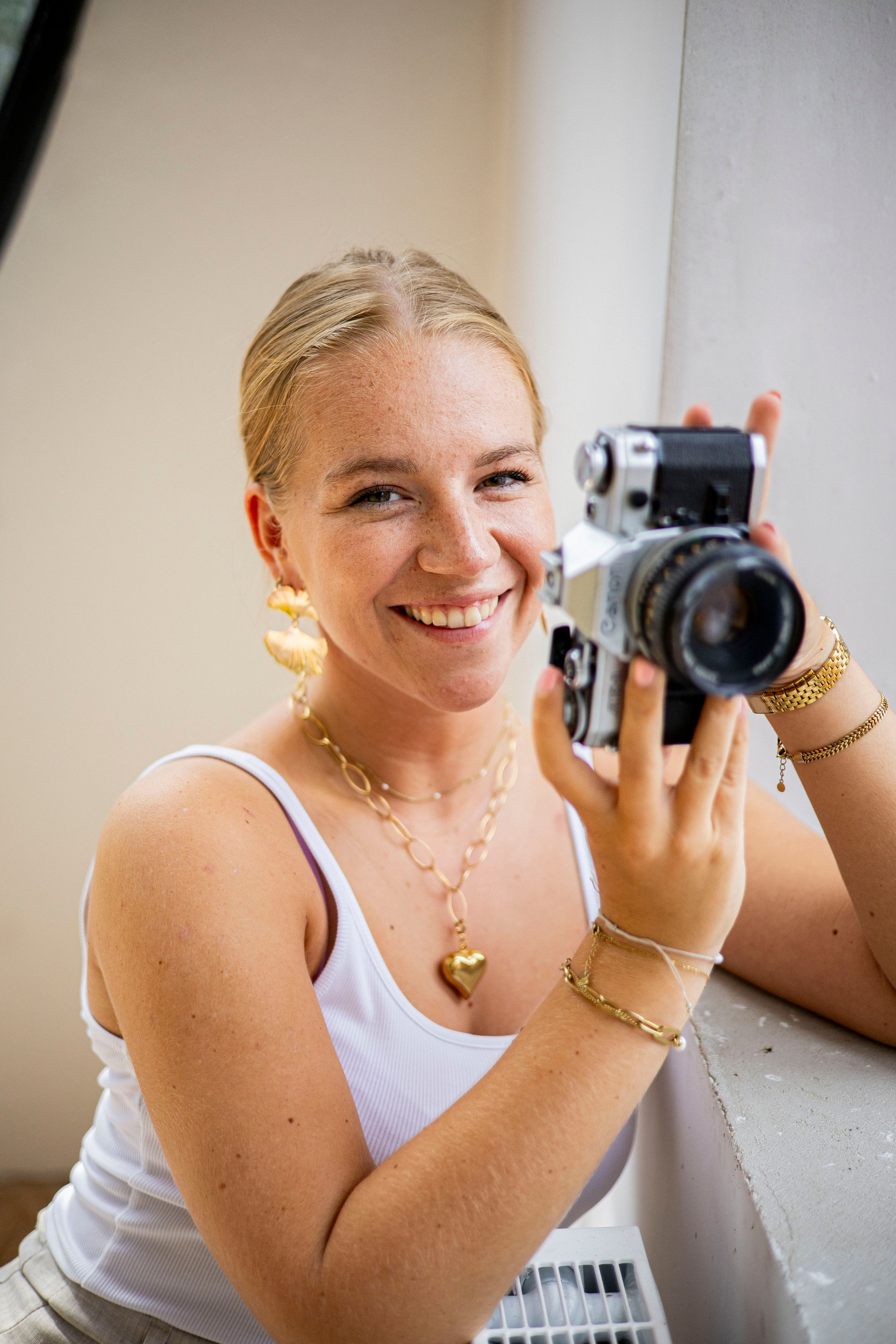 Happy woman with a vintage camera, posing indoors by a window.