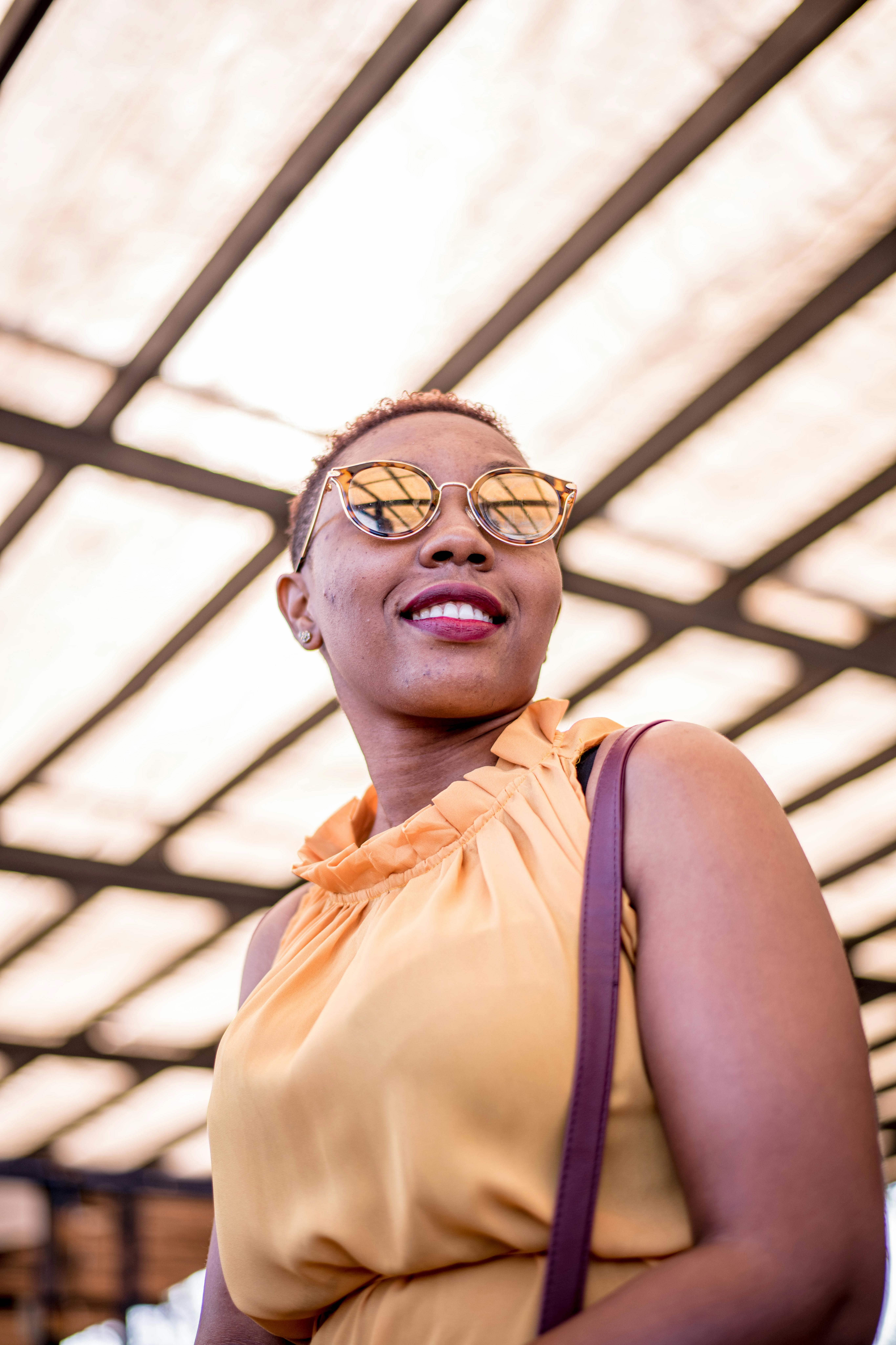 一位戴着墨镜、身穿橙色连衣裙的别致女人，在阳光明媚的天篷下微笑着