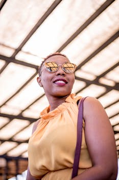 一位戴着墨镜、身穿橙色连衣裙的别致女人，在阳光明媚的天篷下微笑着