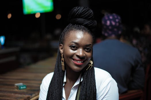 一位留着辫子、面带明亮微笑的黑人女子坐在室内