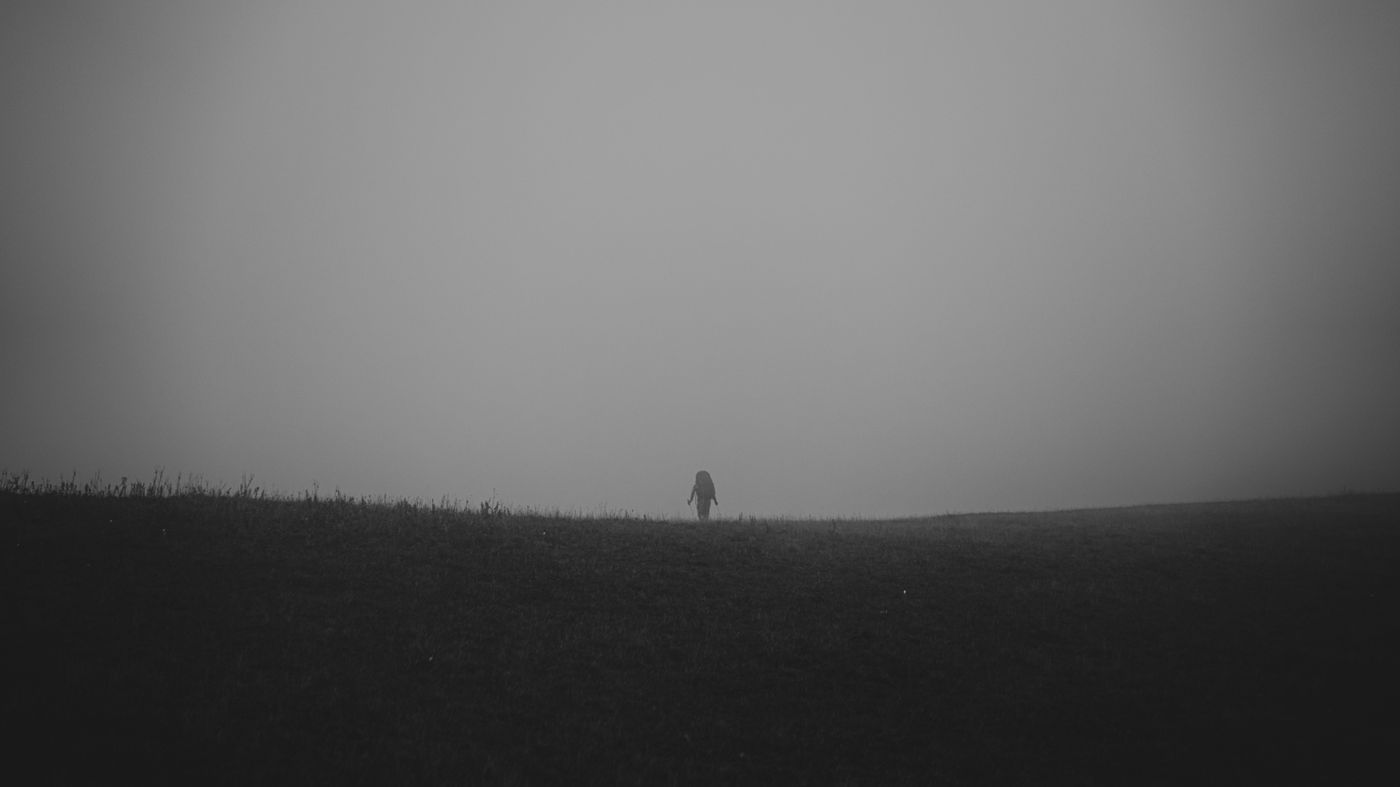 A lone figure standing in a misty, desolate field — photo by ICXOD on Pexels