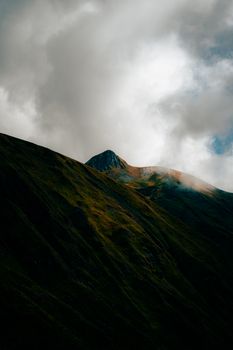Stunning view of a rugged mountain peak with dark slopes and dramatic clouds overhead.