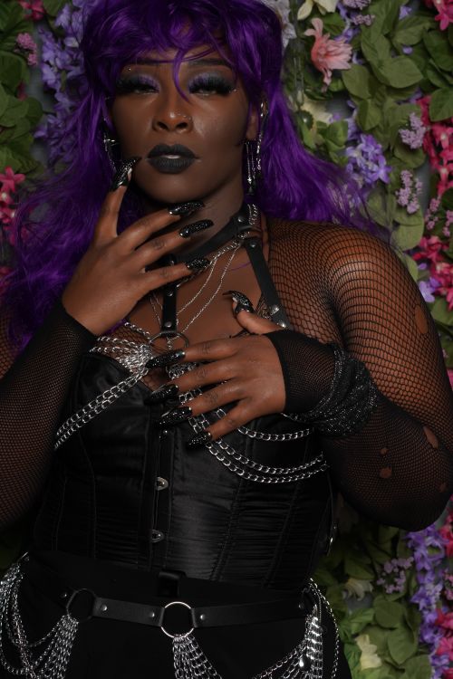 Free A striking gothic fashion model poses with a floral backdrop, showcasing purple hair and black attire. Stock Photo