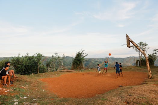 Boys enjoying a basketball game on a rustic outdoor court amidst scenic hills.