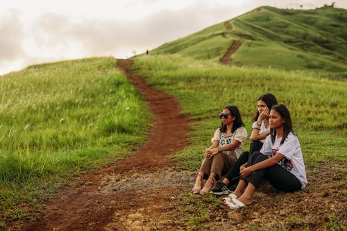Free Three friends sitting and enjoying nature on a scenic green hill path during the day. Stock Photo