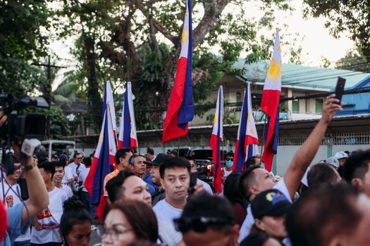 A lively outdoor gathering with people holding Philippine flags, showcasing national pride.