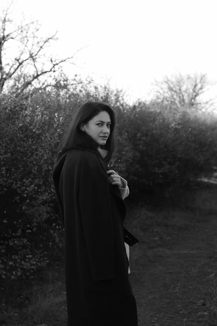 A woman in a coat walks through a winter landscape, captured in black and white.