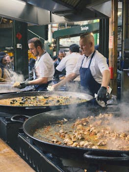 Chefs prepare seafood and chicken dishes in large pans at Borough Market, London.