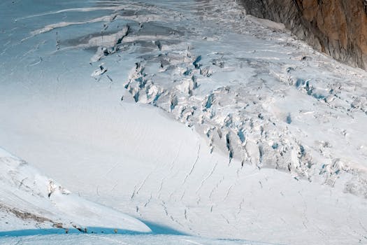 A breathtaking aerial shot of a snow-covered mountain with visible crevices, under clear daylight.