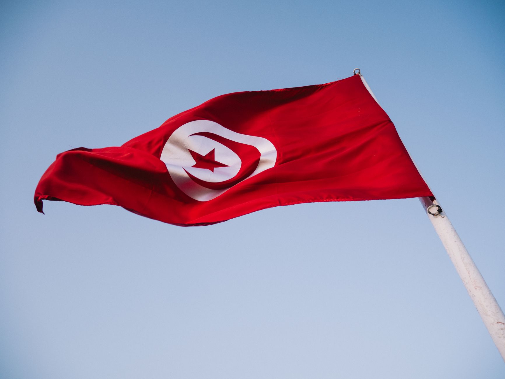 High-quality image of the Tunisian national flag majestically waving against a clear blue sky.