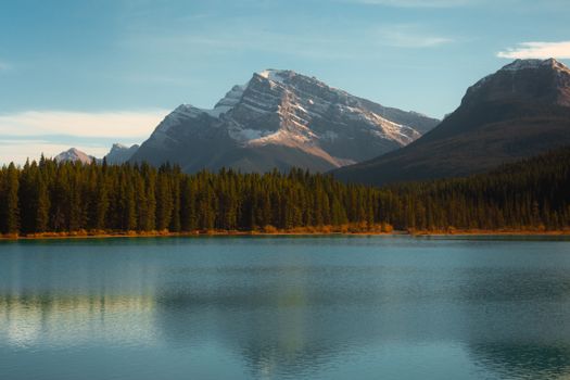 Breathtaking view of a mountain range, pine forest, and serene lake under a clear blue sky.