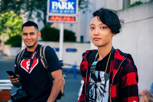 Two young adults in casual attire interacting outdoors on a sunny day. Urban backdrop.