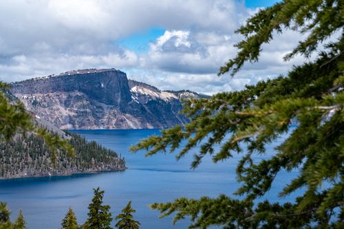 Free Breathtaking view of Crater Lake surrounded by evergreen trees under a bright summer sky. Stock Photo