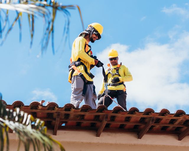 Roofers working on a tile roof Two construction workers in safety gear working on a tiled roof
