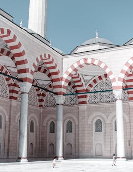 在晴朗的天空下，美丽的清真寺外观展示着红色和白色的拱门、圆顶和圆柱