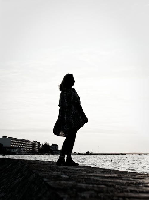 Silhouette of Woman Standing Beside A Body Of Water