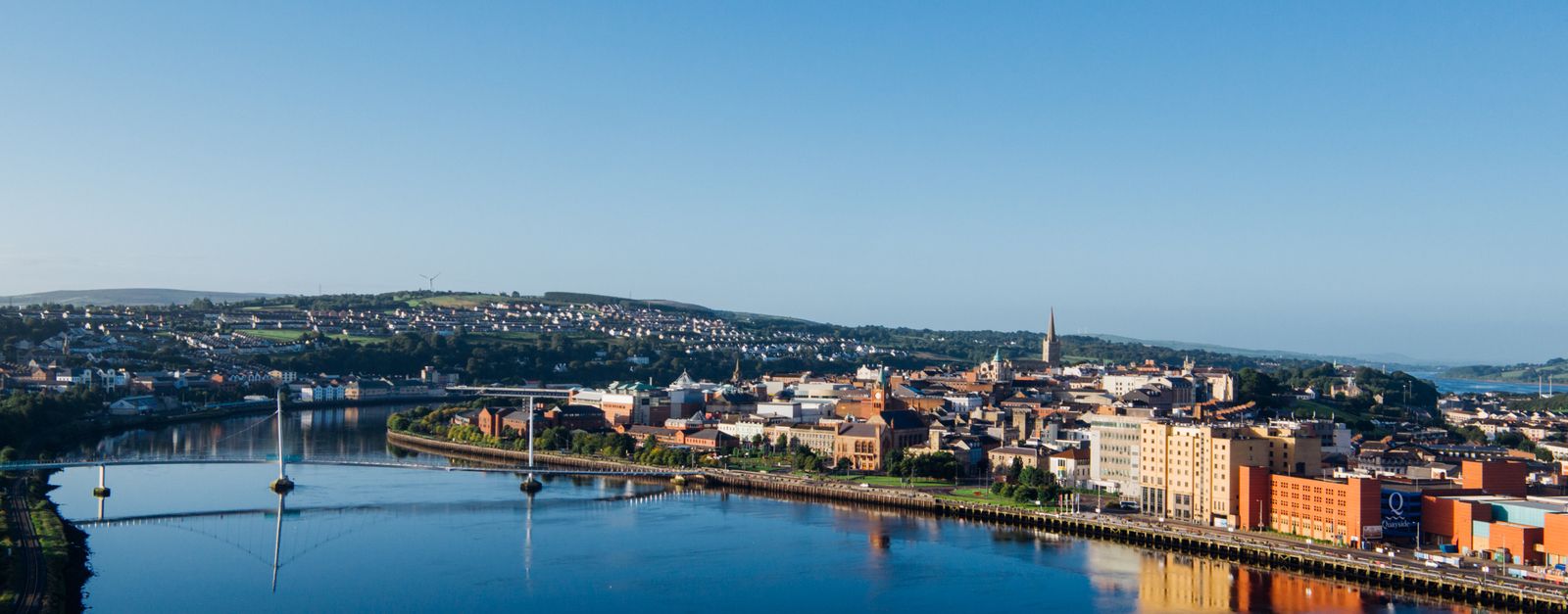 Aerial shot of Derry city and Peace Bridge over River Foyle at sunrise.