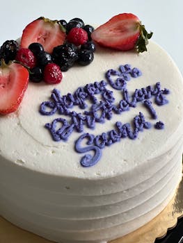 White birthday cake with berries and purple icing, topped with custom text for a 6th birthday.